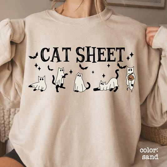 Close-up of the graphic design on a maroon sweatshirt showing detailed illustrations of spooky white ghosts and cats alongside sparkles and stars.