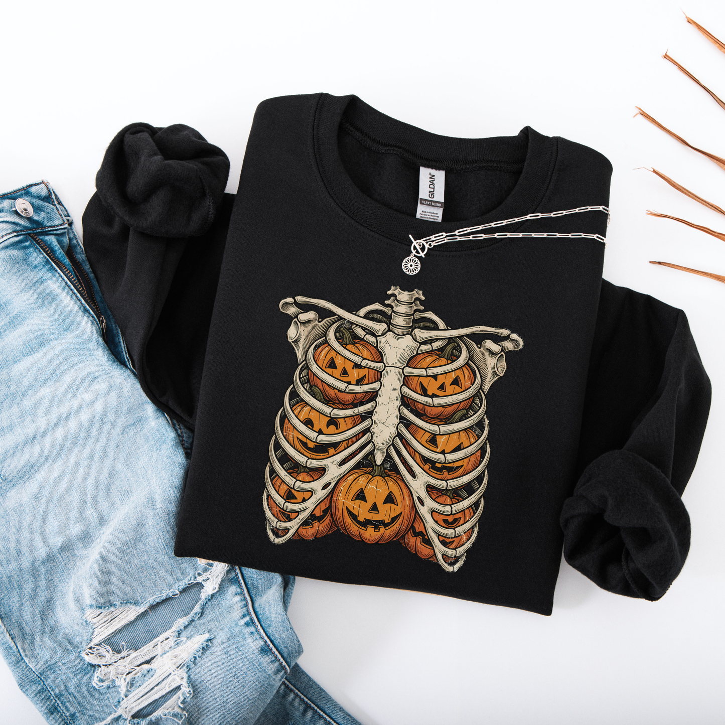Flat lay of a black-colored graphic sweatshirt showcasing a black printed skeleton ribcage with an orange jack-o'-lantern glowing inside the center.