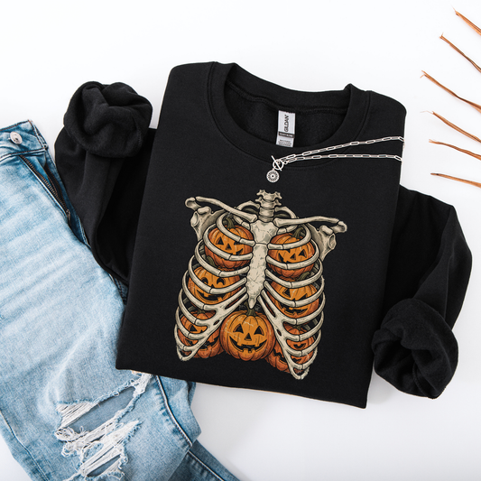 Flat lay of a black-colored graphic sweatshirt showcasing a black printed skeleton ribcage with an orange jack-o'-lantern glowing inside the center.